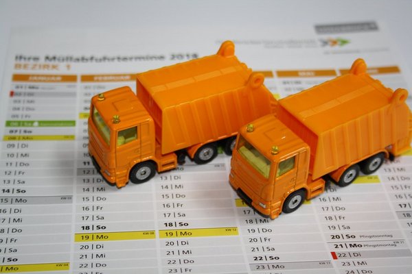 Zwei orange Spielzeug-Müllwagen stehen auf einem Ausdruck des Osnabrücker Müllabfuhrkalenders