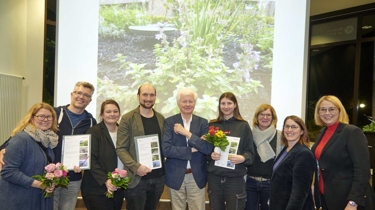 Eine Gruppe von glücklich aussehenden Menschen mit Urkunden und Blumensträußen.