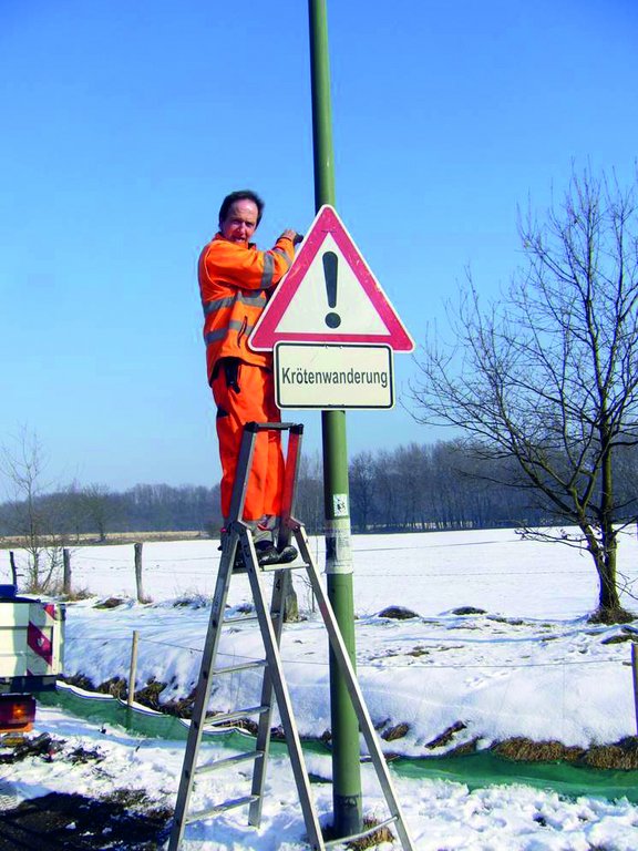 Mitarbeiter vom OSB montiert ein Schild mit der Aufschrift Krötenwanderung